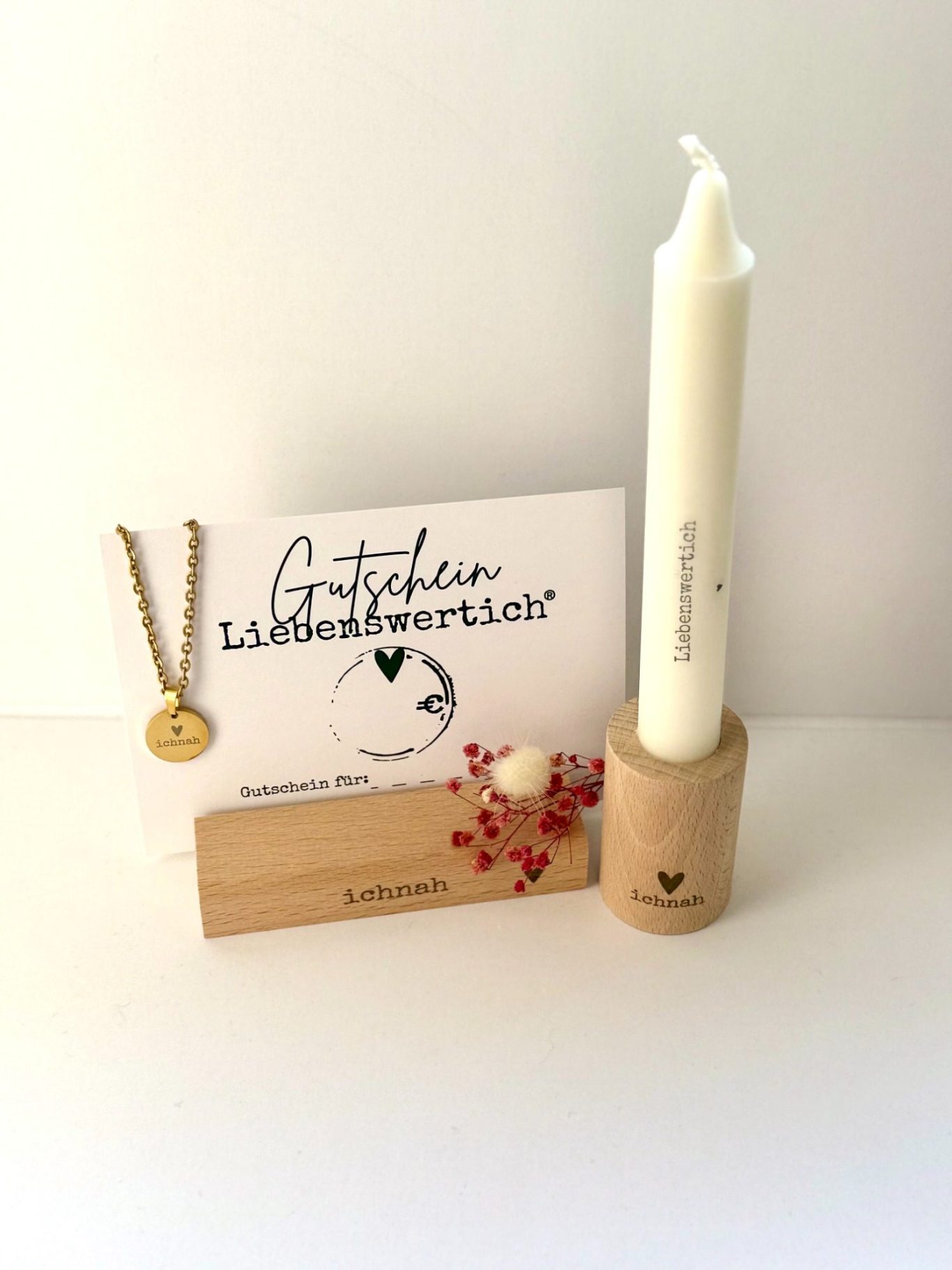 Gutschein Liebenswertich Zarte Dekoration mit einer weißen Kerze, Kette und Karte auf einem Holzständer.
