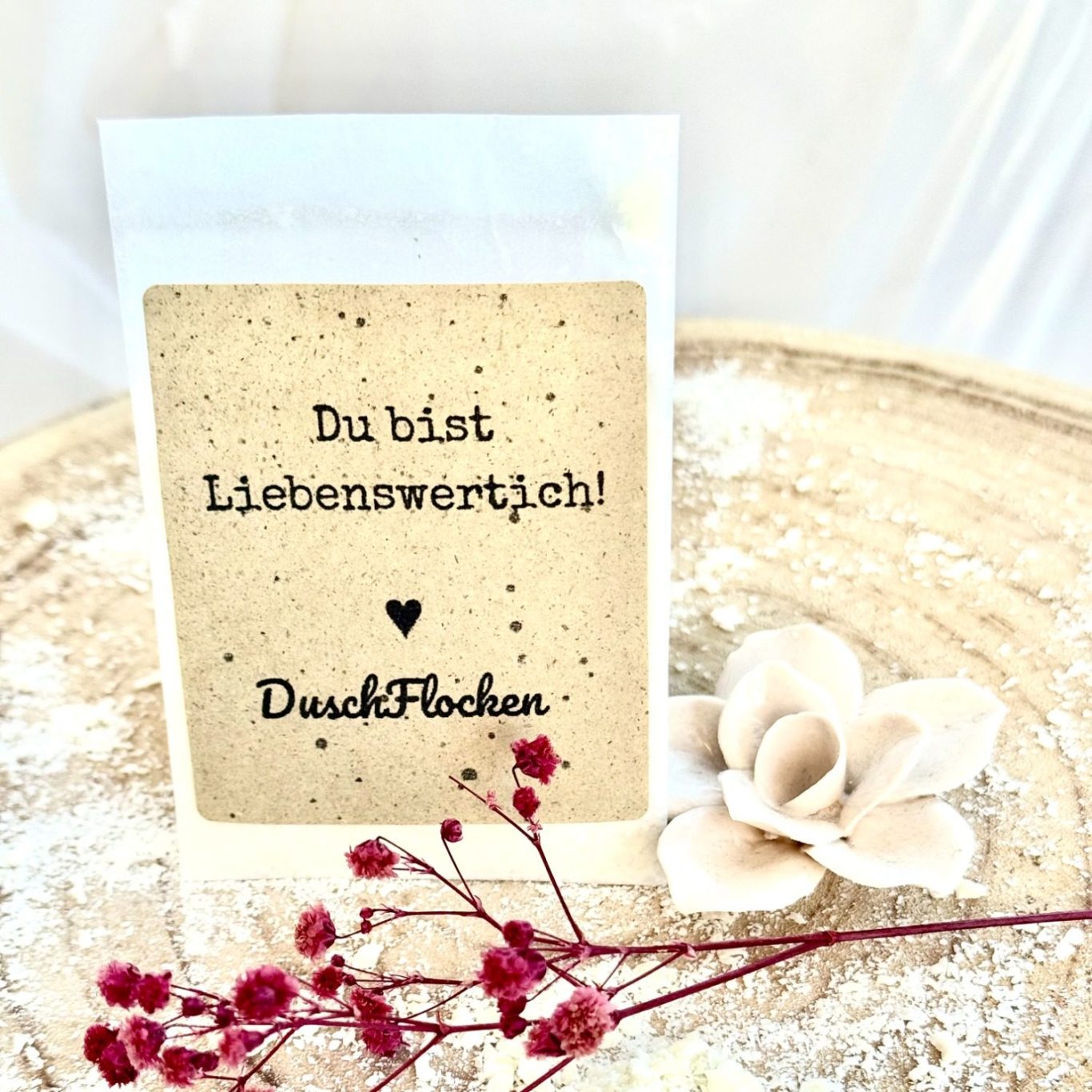 Duschflockenverpackung Ein Karton mit der Aufschrift "Du bist liebenswert!" und einer Blume.